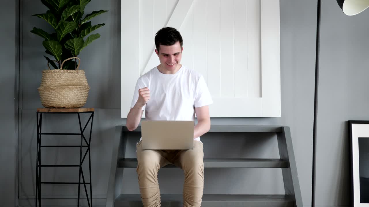 계단에 앉아서 노트북에서 승리를 축하하는 흥분한 남자