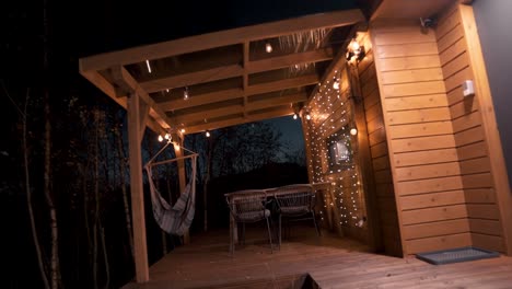 acogedor balcón de cabaña de madera con hamaca y luces cálidas por la noche