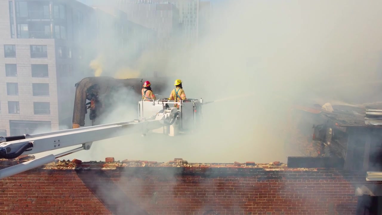 Scena di emergenza antincendio con vigili del fuoco al lavoro su un tetto fumoso e bruciato, Montréal, Canada.