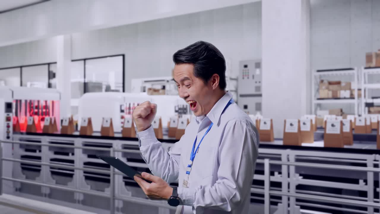 Side View Of An Asian Male Professional Worker Standing With His Tablet With Conveyor for Packaging Coffee Beans in Bags at Coffee Factory, He Raises His Fist Up With Screaming Goal
