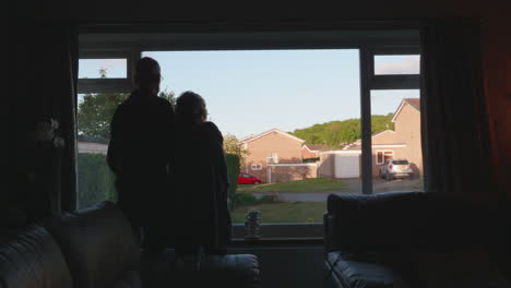 a couple stand looking out of a window on a summer evening as the camera moves back