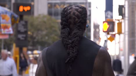 afroamerican black man with long dreadlocks hair walking and listening to music in slow motion in new york city, manhattan, with the radio city music hall in the background