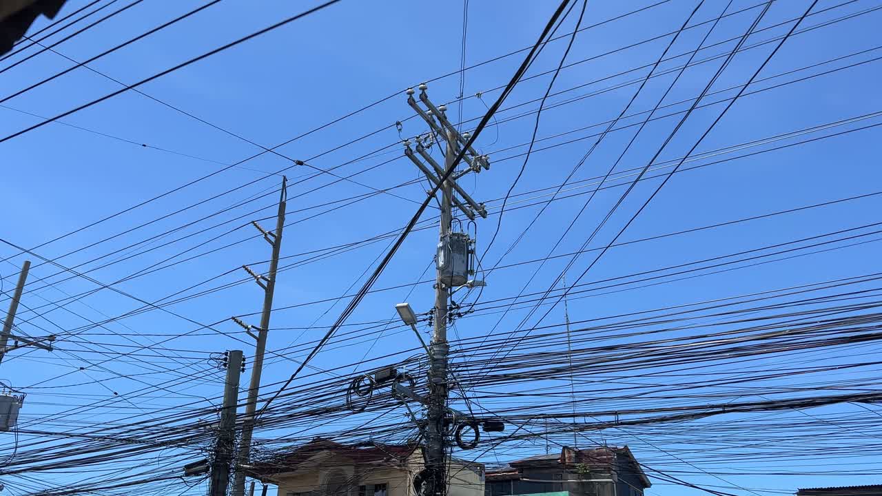 Dense network of tangled electrical wires and transformers fill the sky above a city street—perfect for infrastructure, energy, and technology themes