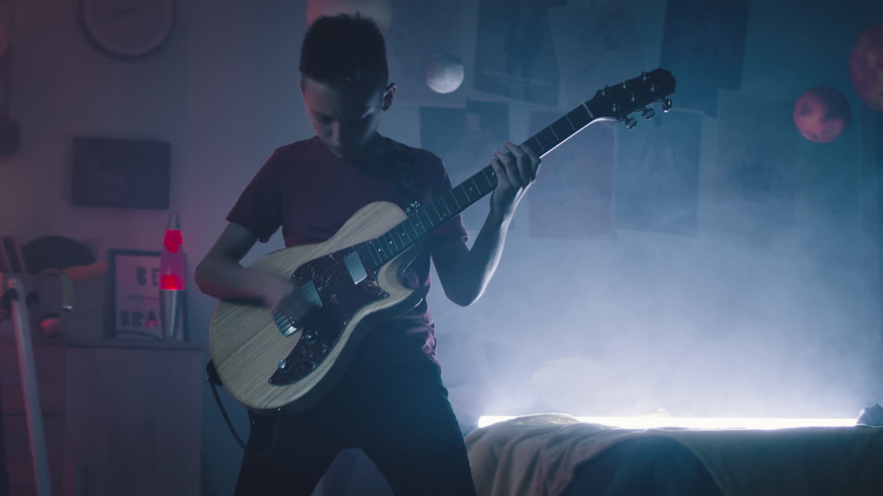 Teenage boy playing guitar in a dimly lit bedroom