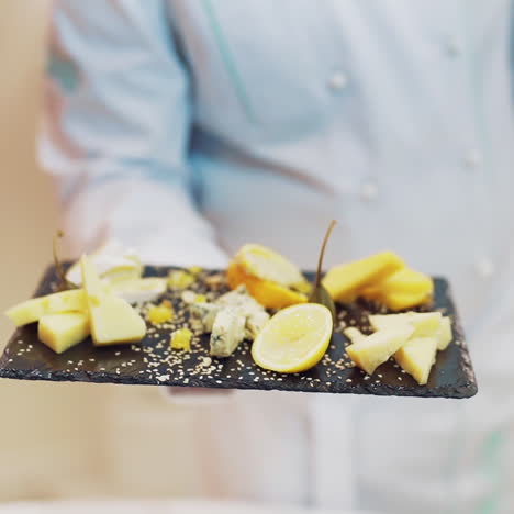 professional chef in white clothes decorates the dish with lemon on the black board. different kinds of tasty cheese nicely presented by cook in the restaurant.