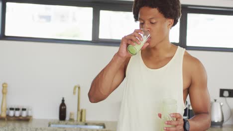 fit african american man cooking, drinking healthy green smoothie