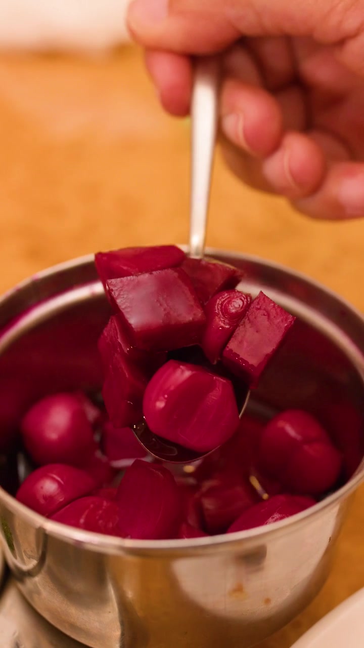 Close-up of hand using spoon to scoop pink pickled onions in a restaurant setting.