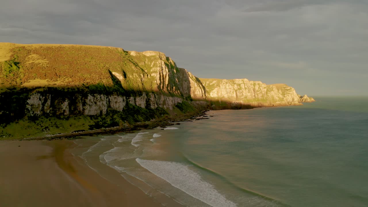 Aerial shot of sunrays hitting the cliffs during sunset along a coastline in New Zealand
