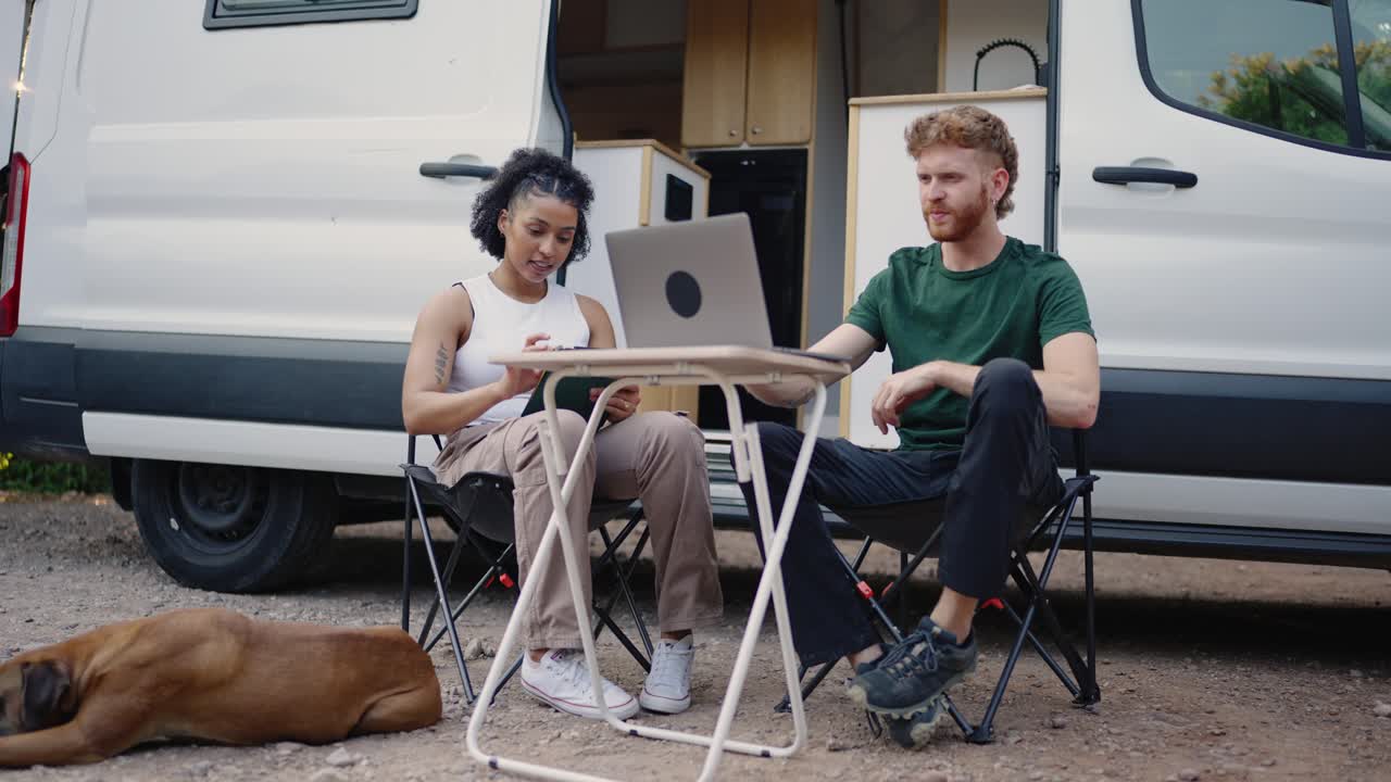 Couple working remotely outside their van with their dog