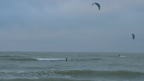 un grupo de personas dedicadas al kitesurf, día de invierno nublado, olas altas, playa de karosta del mar báltico, cámara lenta, plano general