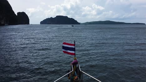 thai flag blowing in the wind as boat cruises past the phi phi islands on sunny day