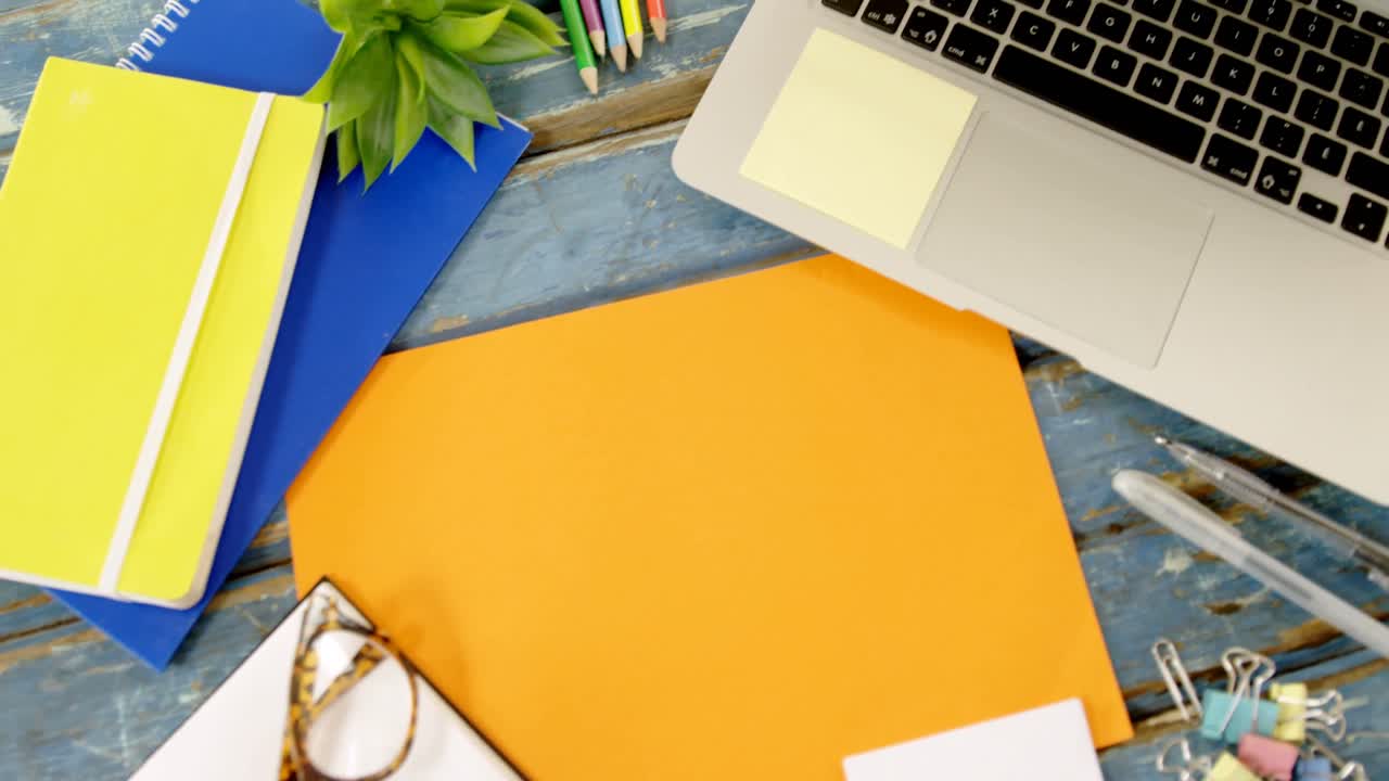 computadora portátil, gafas y varios suministros de oficina en una mesa de madera 4k