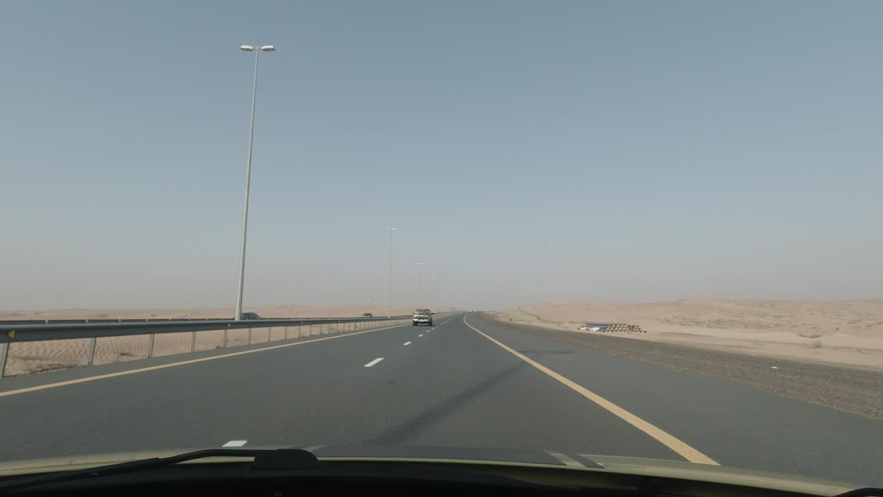 Fast driving on a UAE desert road where some pipes lay along the road with a green garbage compartment. Uneding view of desert sand and almost no vegetation on sight.