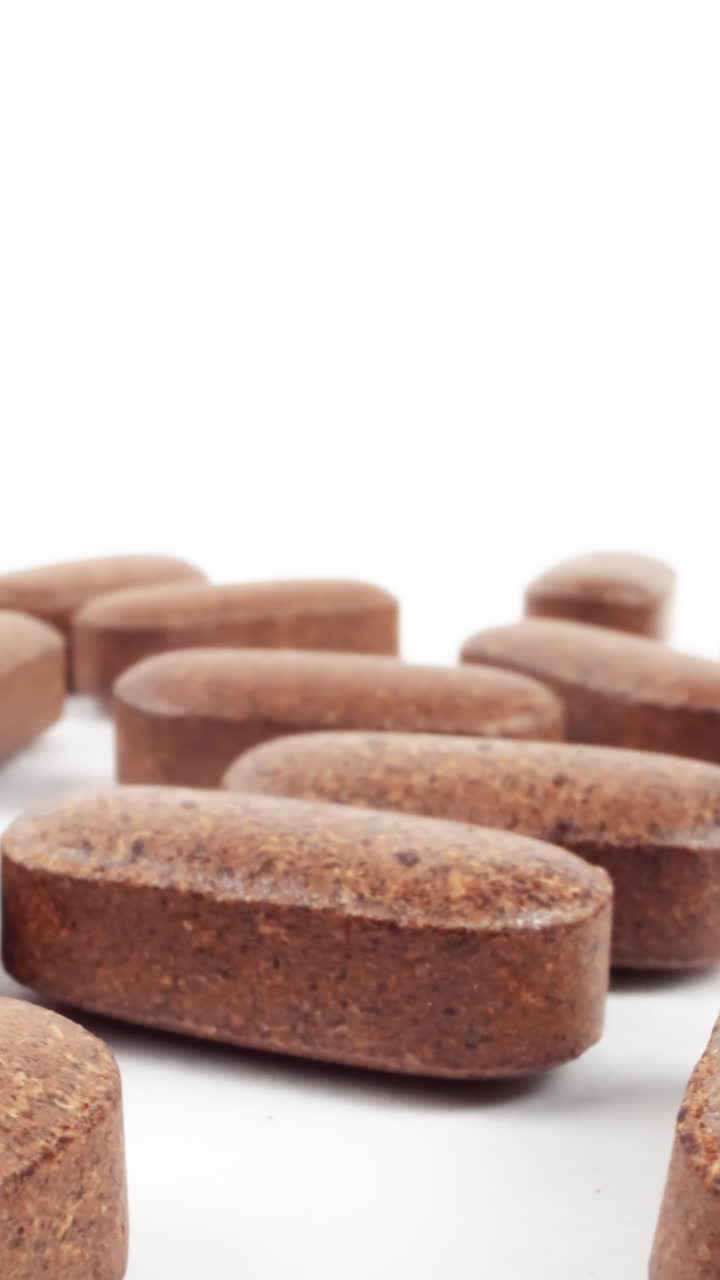 Close-up of brown, textured herbal supplement pills on a white background