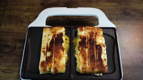 female opens a white hot-pressed sandwich machine with two cheese sandwiches heating up inside, then takes out one sandwich with a fork