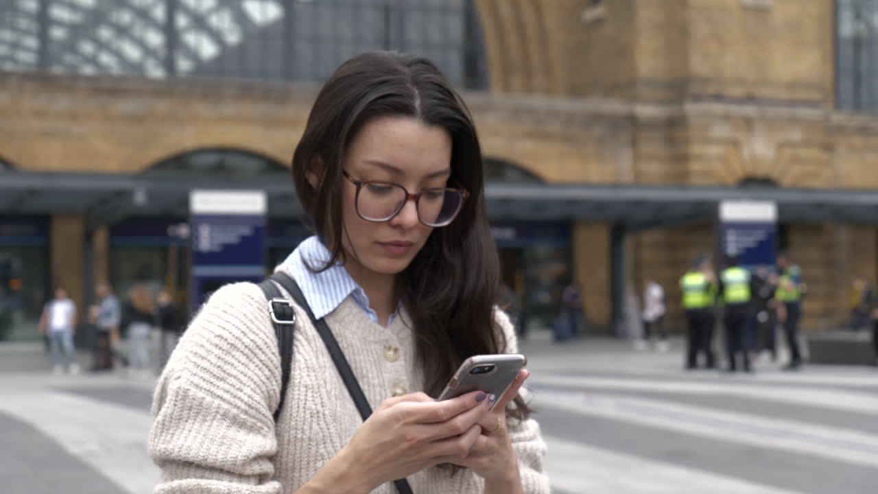 Young professional business woman stood outside London Kings Cross train station using her smartphone