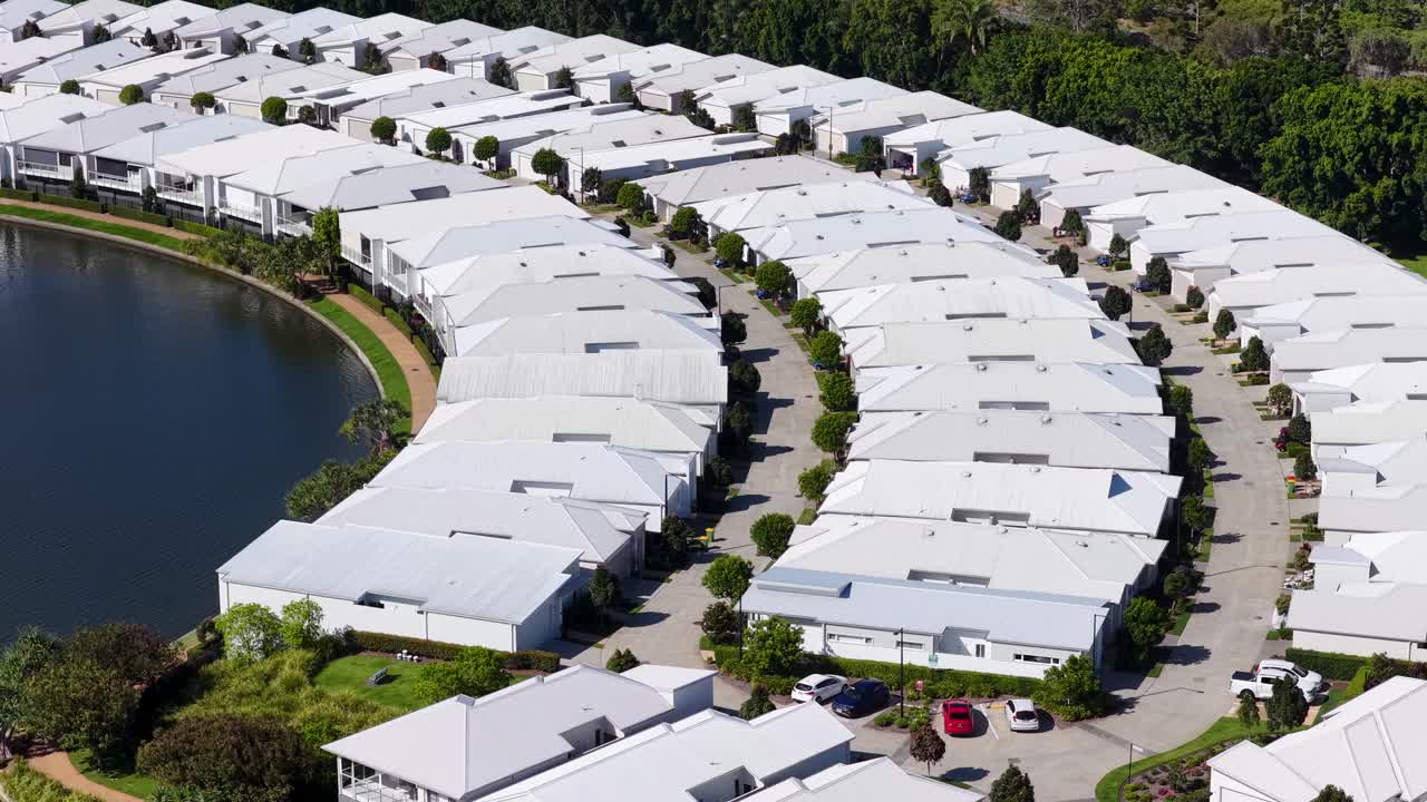 Drone glides above curved lakeside residential neighborhood with white roofs in bright daylight