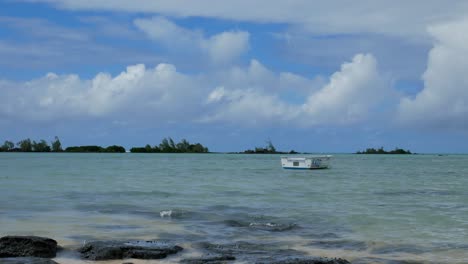 Eine-Idyllische-Szene-Eines-Kleinen-Bootes-In-Einem-Hellblauen-Meer,-Unter-Einem-Himmel-Mit-Wunderschönen-Wolken-Auf-Einer-Tropischen-Insel