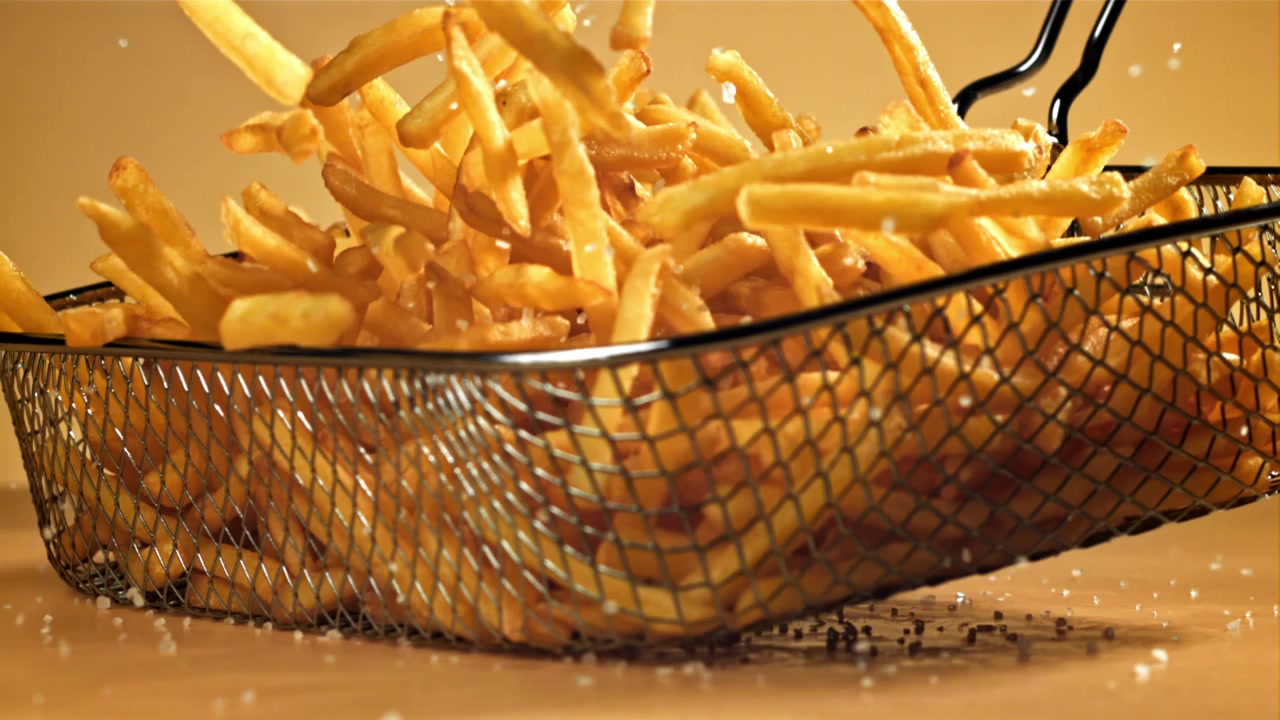 In Zeitlupe fällt Salz auf heiße Pommes frites in einem Korb