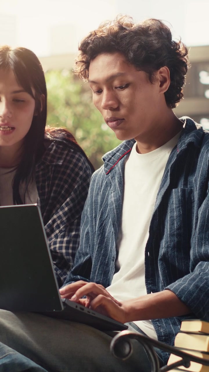 Video verticale: Studenti che esaminano insieme un progetto sul laptop su una panchina del campus.
