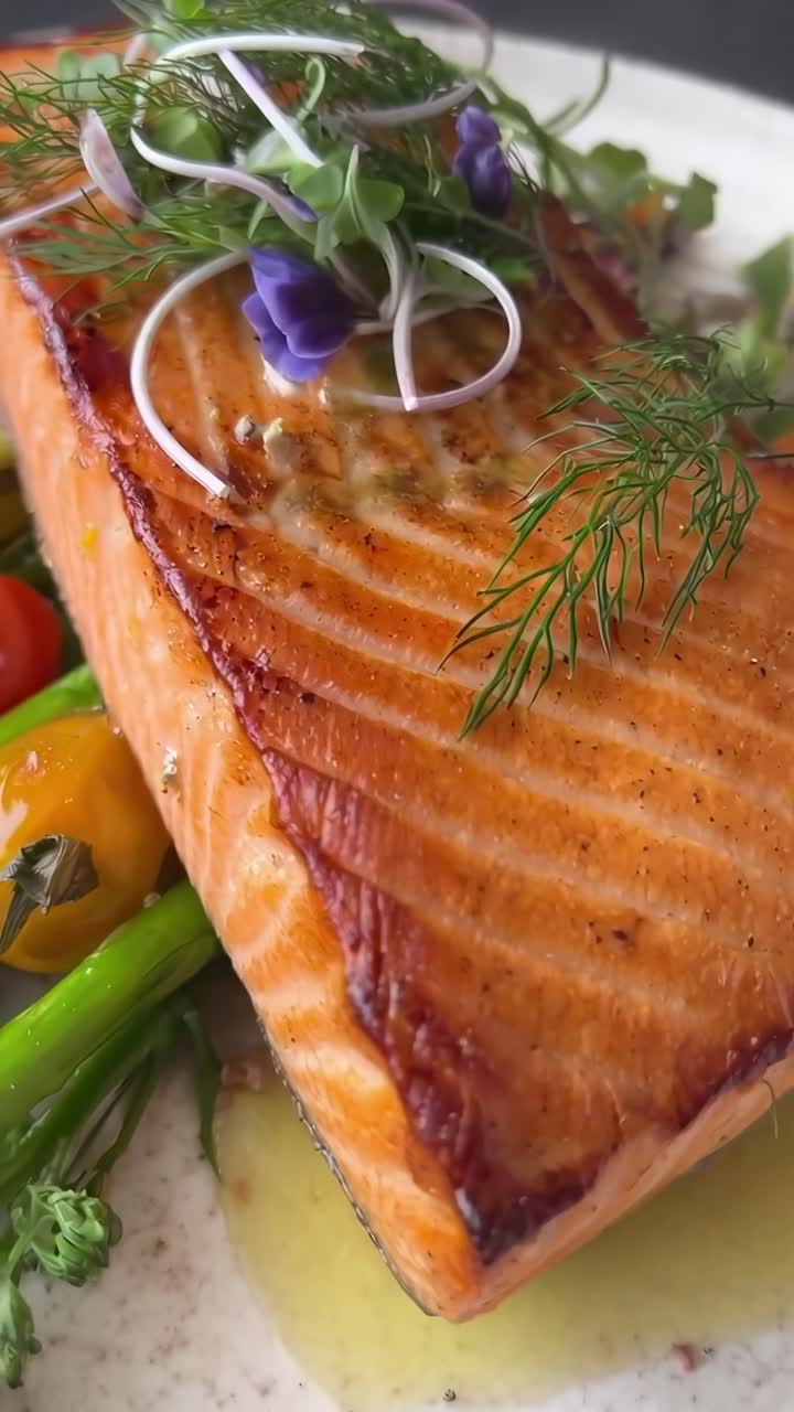 Video ravvicinato di un piatto gourmet a base di salmone con verdure dai colori vivaci, ripreso da un angolo dall'alto