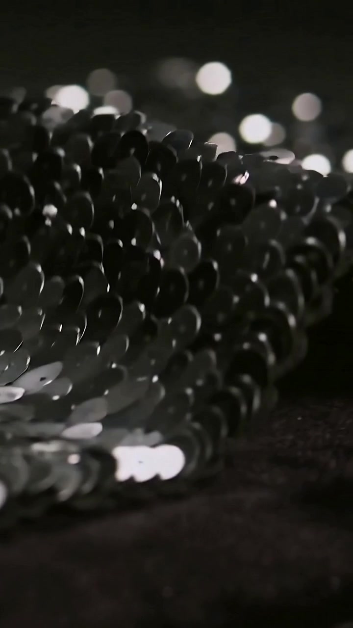 Video verticale: Telecamera panoramica che rivela paillettes metalliche su tessuto scuro in studio, mostrando l'effetto bokeh.
