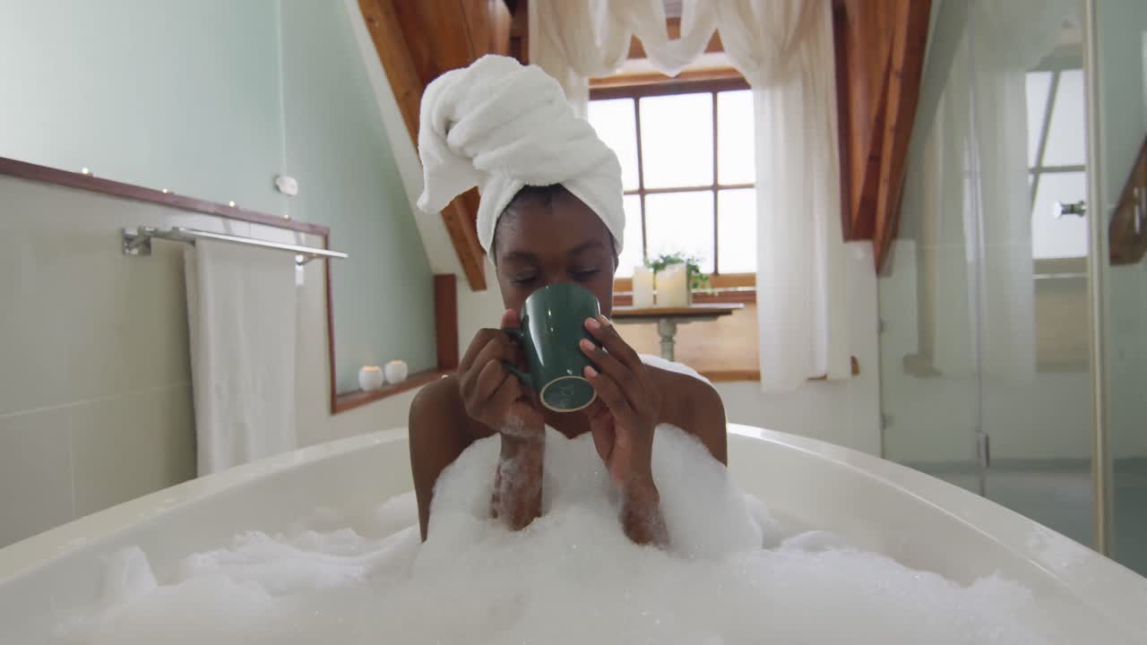 African american attractive woman relaxing in foam bath and drinking coffee in bathroom