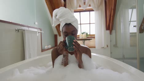 mujer afroamericana atractiva relajándose en el baño de espuma y bebiendo café en el baño