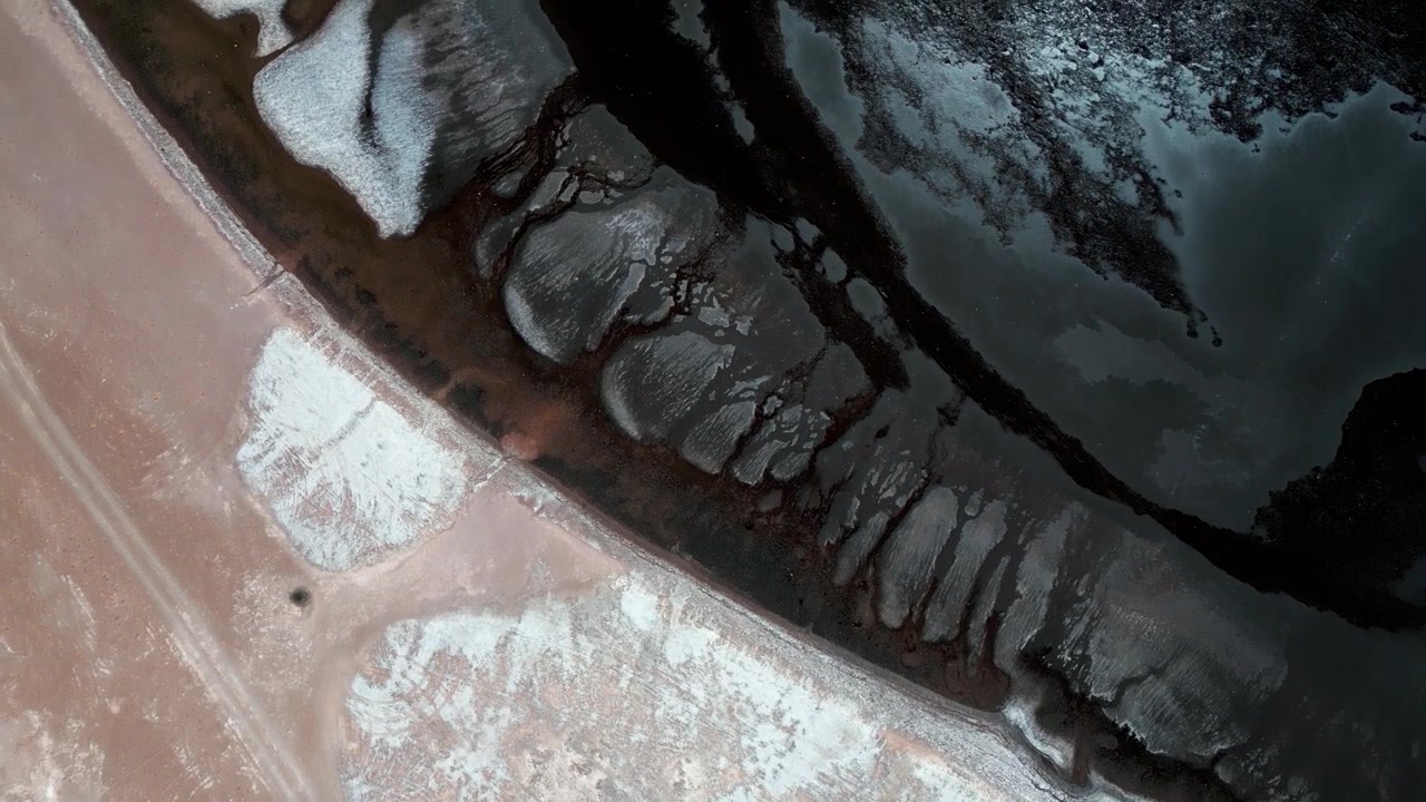 Top down aerial view of Laguna Tara dark water shoreline with abstract white salt crust patterns and sandy sediment creating dramatic natural contrast. Laguna Tara, San Pedro de Atacama, Chile