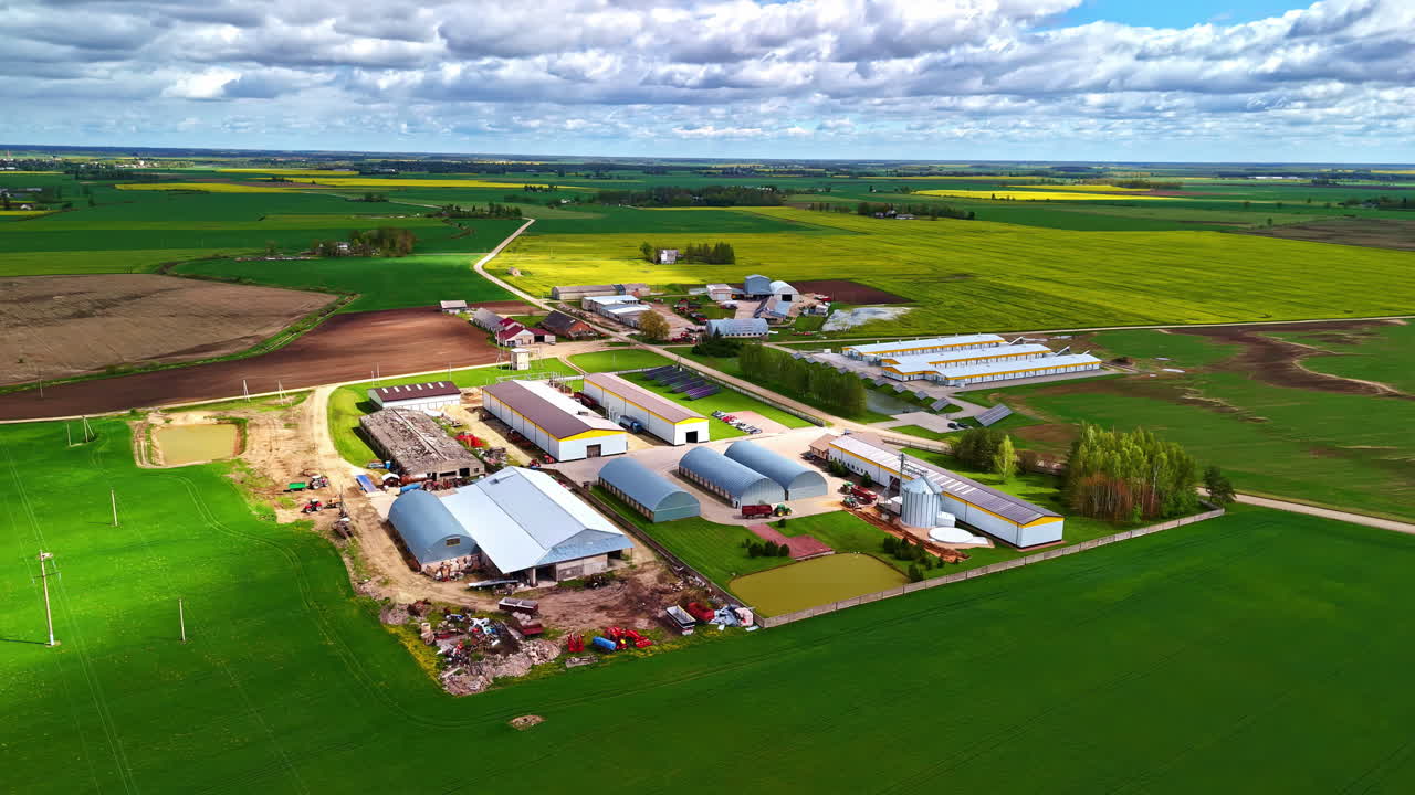 High aerial footage above an industrial agricultural plant amidst green fields.