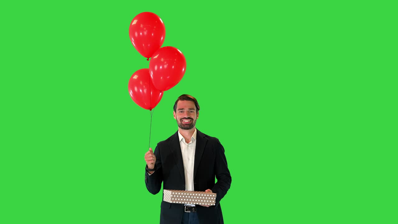 선물 상자와 풍선과 함께 우아한 슈트를 입은 잘생긴 남자가 녹색 화면에서 고, 크로마 키