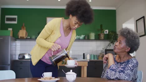 Happy-african-american-adult-daughter-and-senior-mother-having-coffee-talking-at-home,-slow-motion