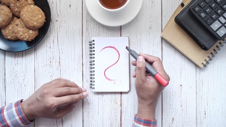 Person writing a question mark in a notebook
