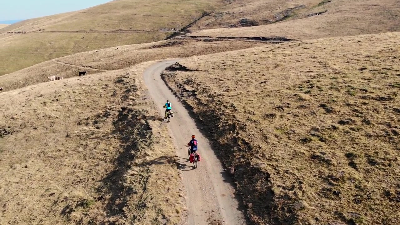 Aerial: two mountain bikers going downhill in a high mountain deserted area in summer time