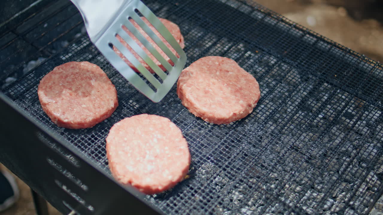 Raw burger patties grilling on barbecue at forest picnic closeup. Unknown person