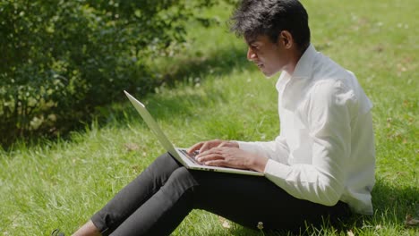 Profile-view-of-young-man-working-remotely-with-laptop-at-park,-sunny-day