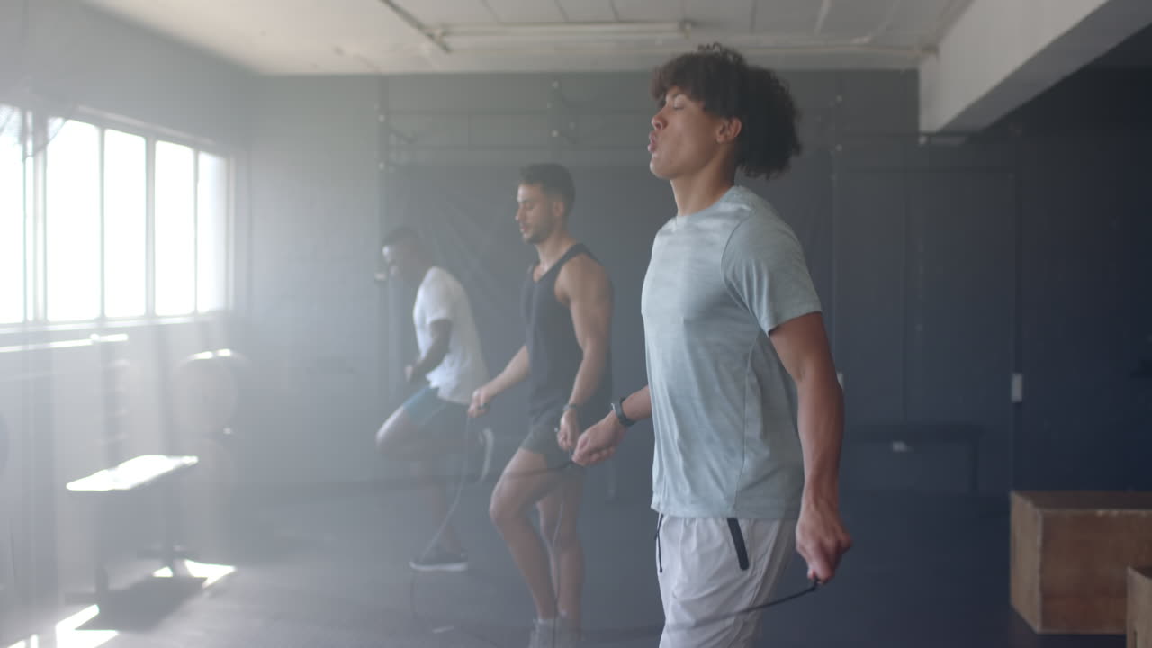 Diverse young men training with jump ropes in gym, wearing athletic clothing