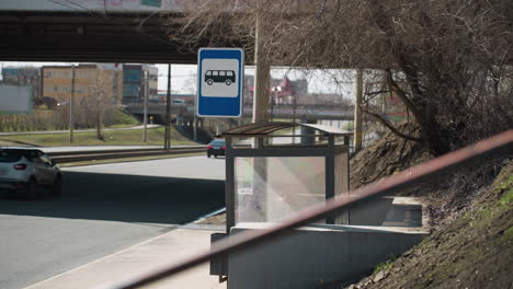 close view of two persons passing by, with a bus stop sign in an urban setting, it captures a bus stop sign with a road and passing cars in the background