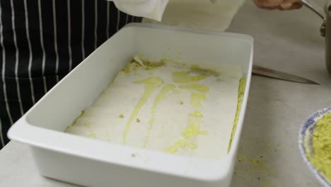 Adding-melted-butter-and-chopped-nuts-onto-baklava-dough-layer-inside-ceramic-pan