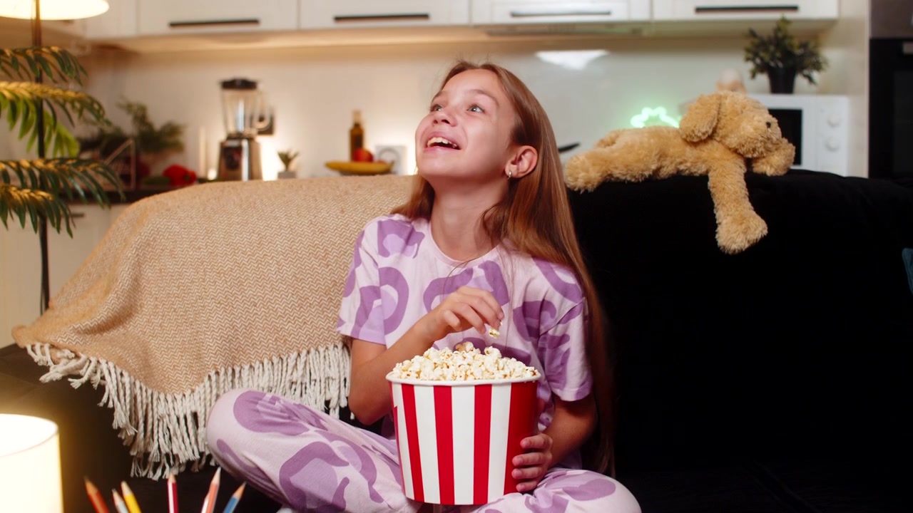Teenagepige ser film, spiser popcorn, griner højt, sjov komedie, munter stemning, weekendstemning, glad