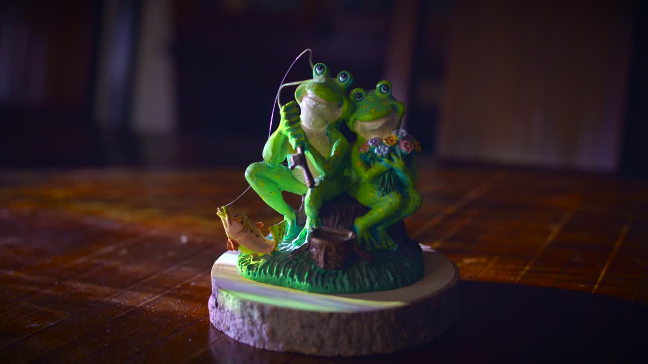 Couple Frog Figurine On Wooden Presentation Base With Lights. Male Frog Holding Fishing Rod While Sitting Next To His Lovely Girlfriend. close up