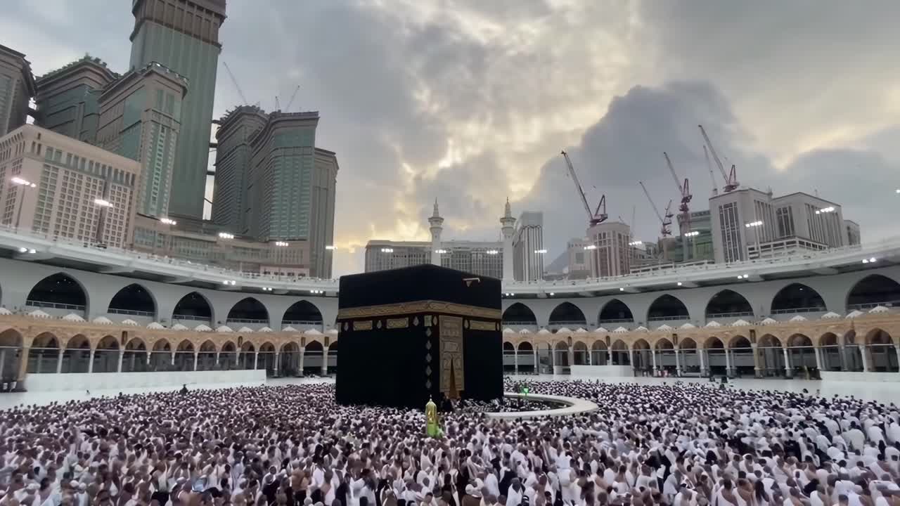 Video grandangolare di pellegrini in bianco che girano intorno alla Kaaba, con imponenti edifici sullo sfondo