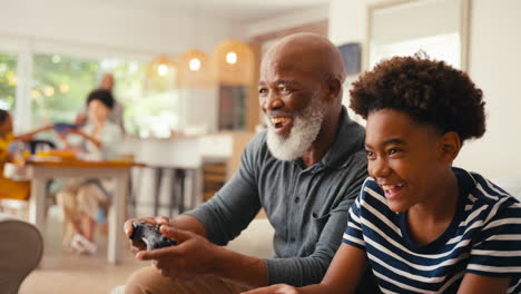 grandfather and grandson sitting on sofa at home playing video game together