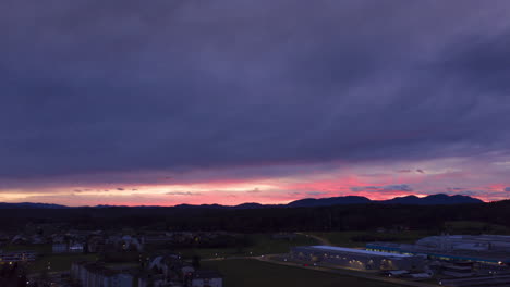 cielo azul oscuro y morado, hiperlapso aéreo, lapso de tiempo de la puesta de sol sobre un pequeño pueblo en europa con rayas de rayos de sol detrás de las montañas