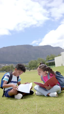 vertical video: in school, children sitting on grass, reading books and smiling outdoors