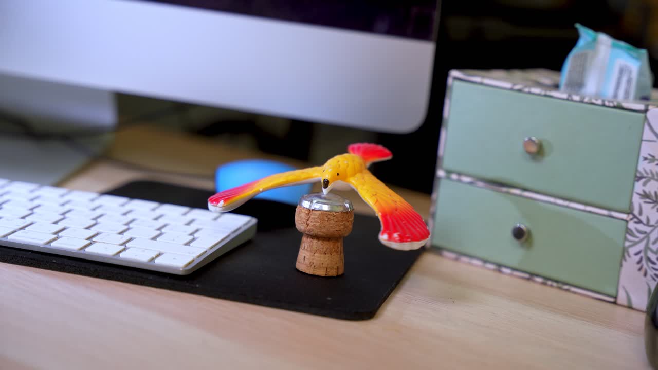 Colorful bird toy balanced on a cork at a modern desk, symbolizing creativity, fun, and personal office aesthetics.