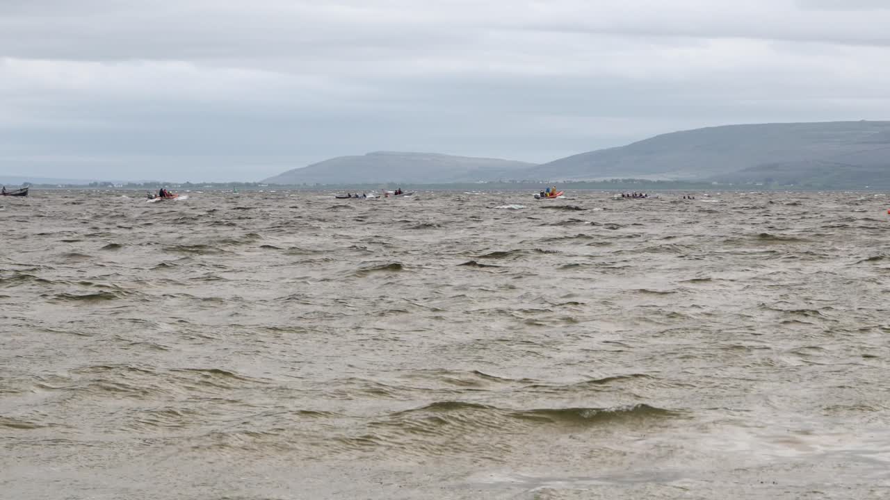 los barcos de currach corren en la distancia de la bahía de galway, el condado de clare detrás