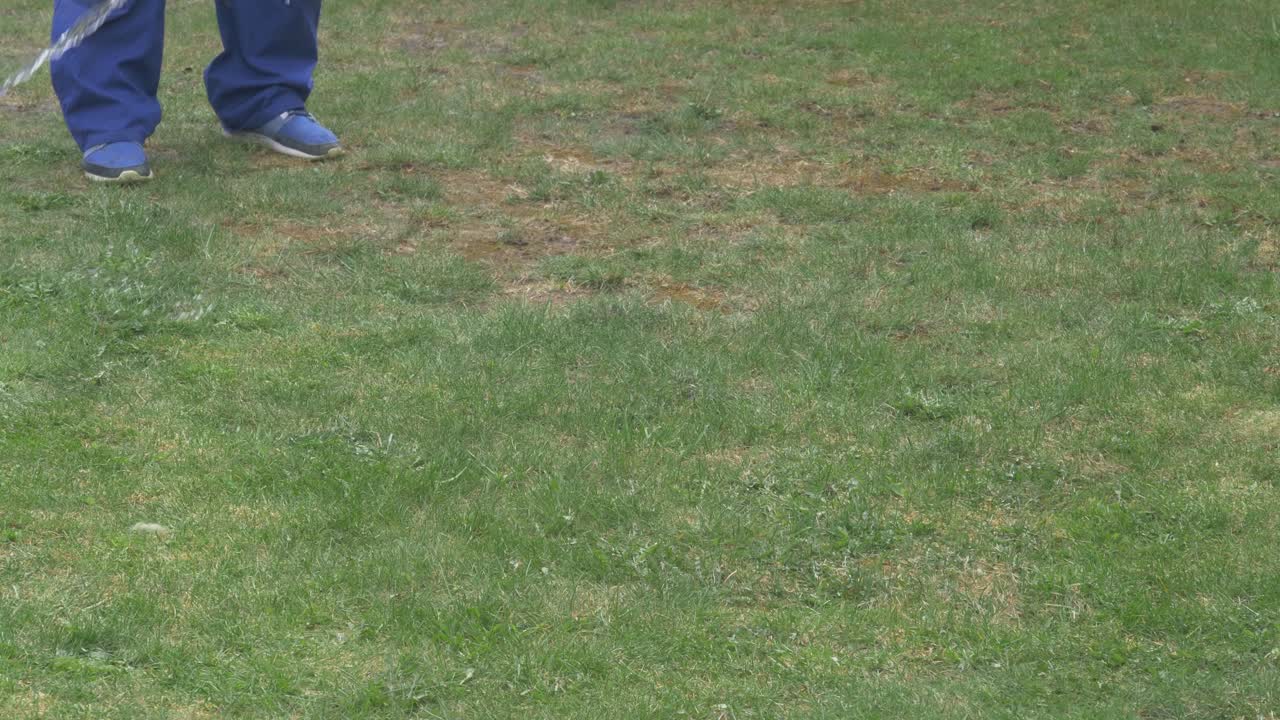 잔디밭에서 마른 풀에 물을 붓는 파란색 옷을 입은 남성 정원사