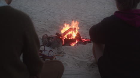 people sitting on sand and warming themselves by the bonfire at the beach in st