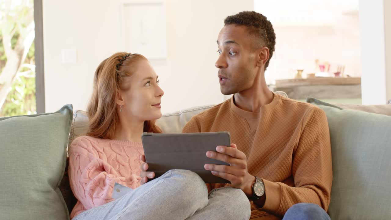 Diverse couple using tablet at home, enjoying cozy holiday time together